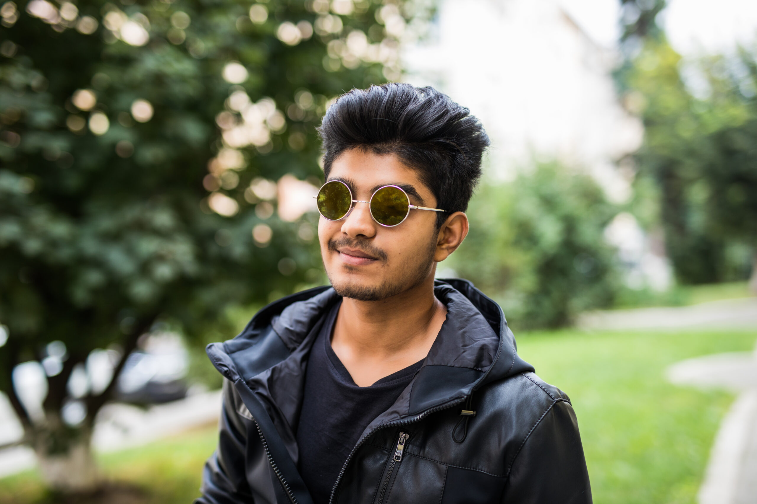 Young Indian man wearing sunglasses while thinking against street outdoors